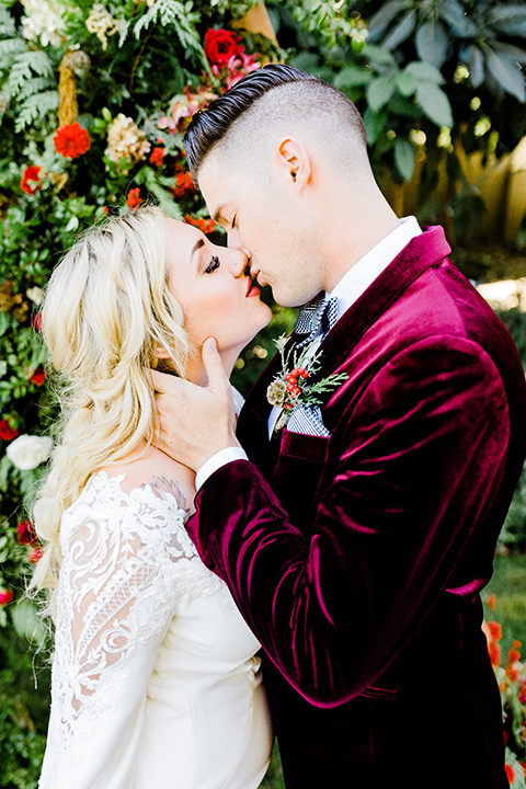  Christmas styled shoot with the groom in a burgundy velvet tuxedo and black pants  and the bride in a white long formfitting gown and long sleeves 