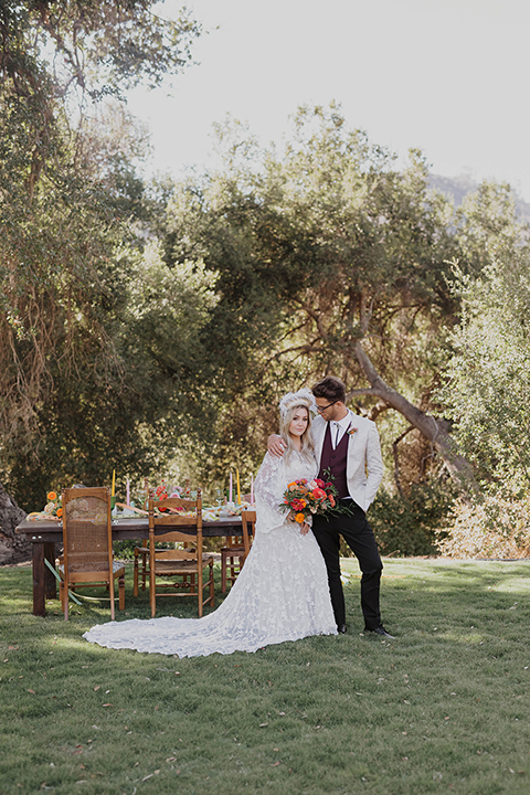  bride in a lace bohemian gown and the groom in an ivory paisley and burgundy ants and a bolo tie 