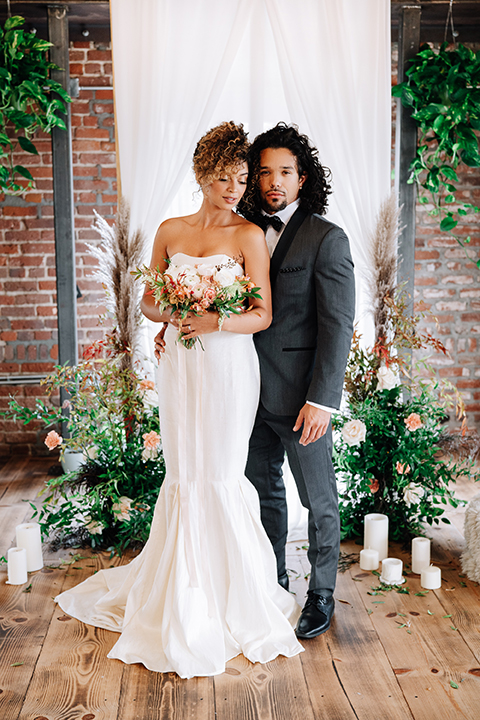  bride in a two-piece gown with her hair in a chic up-do and the groom in a charcoal tuxedo with a black lapel and a black bow tie