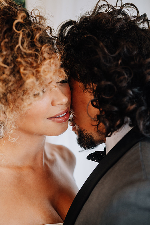  bride in a two-piece gown with her hair in a chic up-do and the groom in a charcoal tuxedo with a black lapel and a black bow tie 