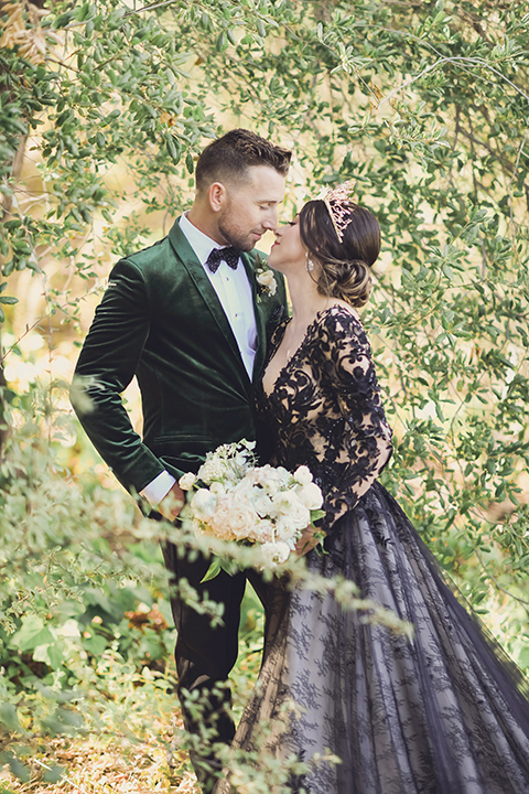  bride in a black lace gown and the groom in a green velvet tuxedo with a black bow tie and shoes 