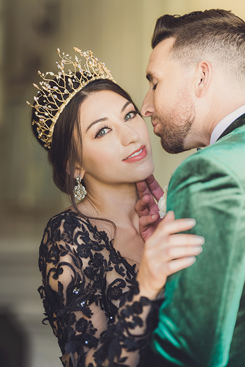  bride in a black lace gown and the groom in a green velvet tuxedo with a black bow tie and shoes 