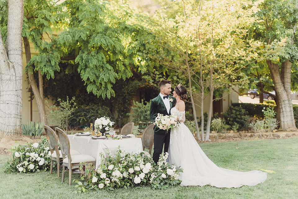  bride in a black lace gown and the groom in a green velvet tuxedo with a black bow tie and shoes 