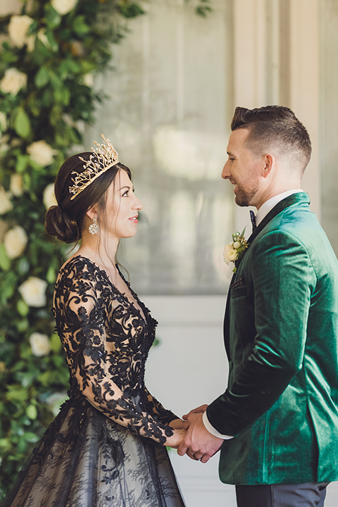  bride in a black lace gown and the groom in a green velvet tuxedo with a black bow tie and shoes 