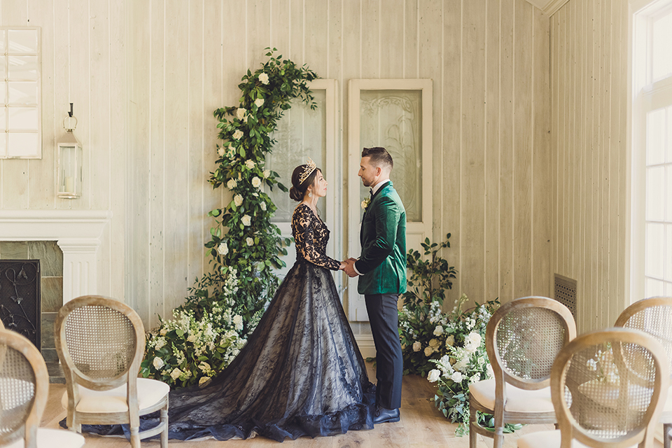  bride in a black lace gown and the groom in a green velvet tuxedo with a black bow tie and shoes 