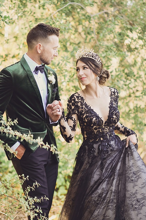  bride in a black lace gown and the groom in a green velvet tuxedo with a black bow tie and shoes 