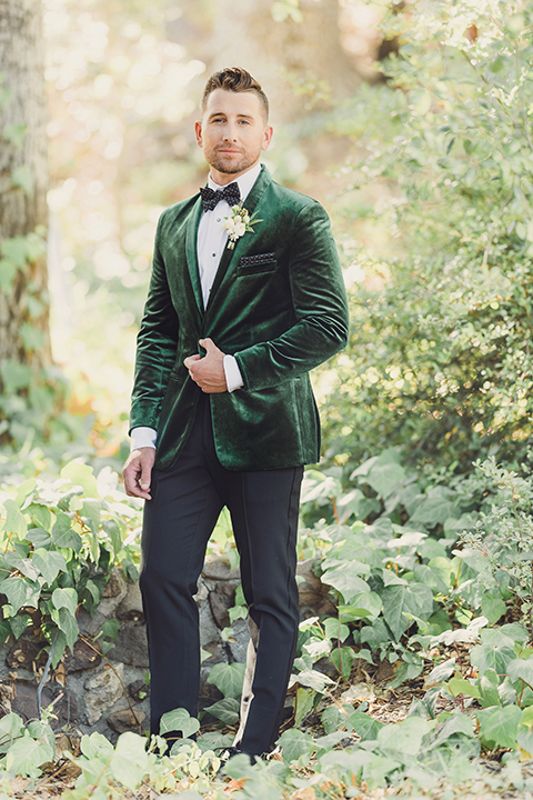  bride in a black lace gown and the groom in a green velvet tuxedo with a black bow tie and shoes 