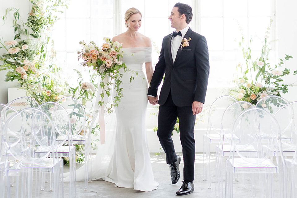  a modern black tie style wedding with the bride in a formfitting gown with a tulle off the shoulder 2 piece wedding gown and the groom in a black tuxedo 