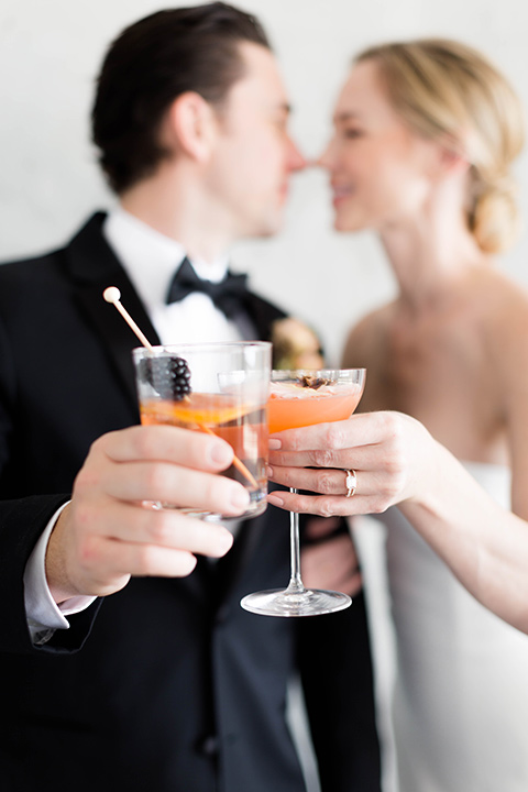  a modern black tie style wedding with the bride in a formfitting gown with a tulle off the shoulder 2 piece wedding gown and the groom in a black tuxedo 