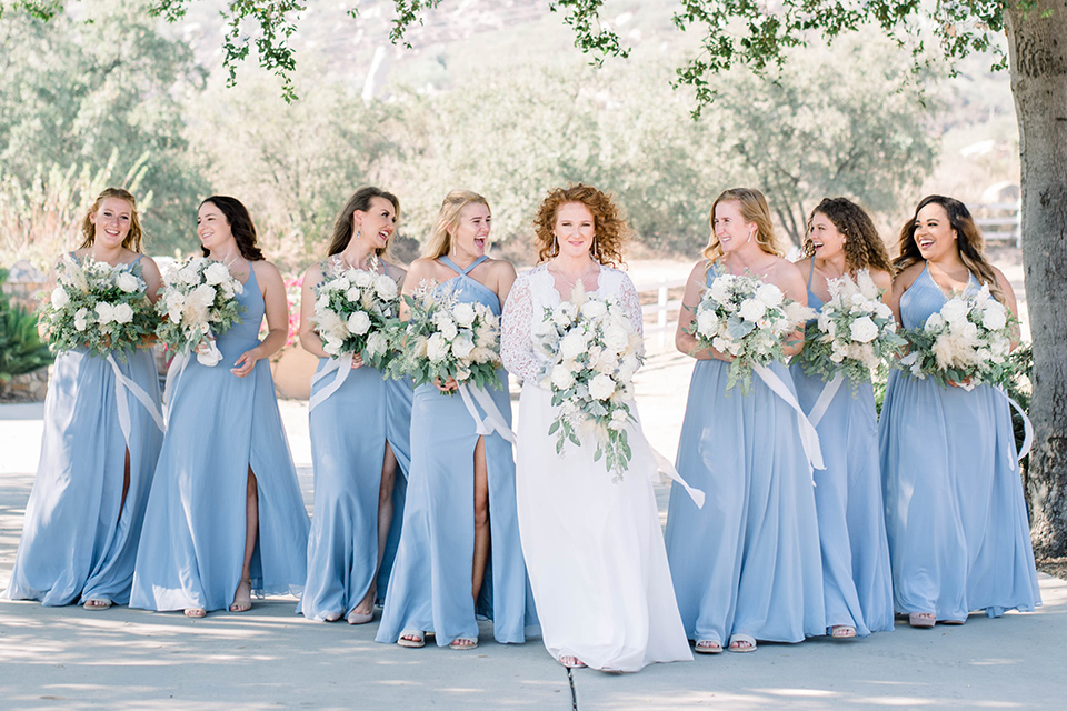  bride in a white lace gown and the groom and groomsmen in ivory paisley tuxedo and the bridesmaids in a light dusty blue gown 