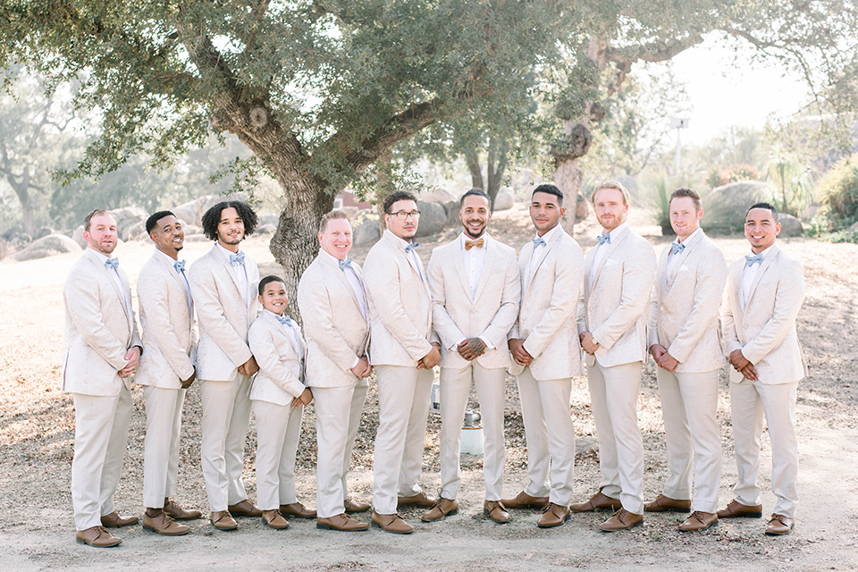  bride in a white lace gown and the groom and groomsmen in ivory paisley tuxedo and the bridesmaids in a light dusty blue gown 