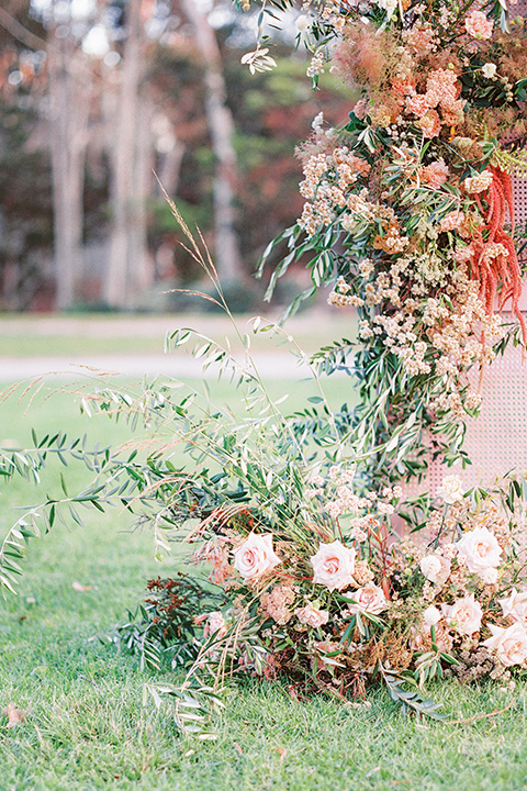  stunning chic pink and yellow wedding very french inspired, the ceremony florals in pinks, golds, greens, and yellows against a light blush pink wood backdrop  