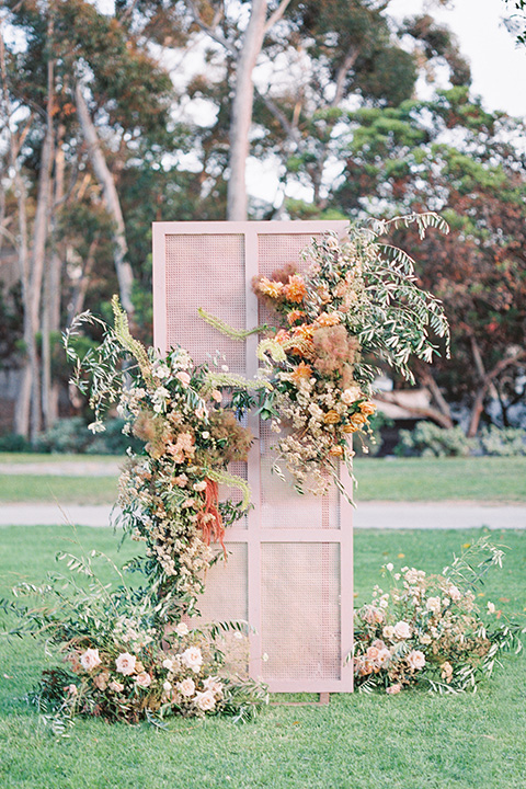  stunning chic pink and yellow wedding very french inspired, the ceremony florals in pinks, golds, greens, and yellows against a light blush pink wood backdrop  