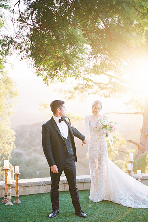  groom wearing black notch lapel tuxedo and the bride in a white fitted gown with a low back detail and lace accents