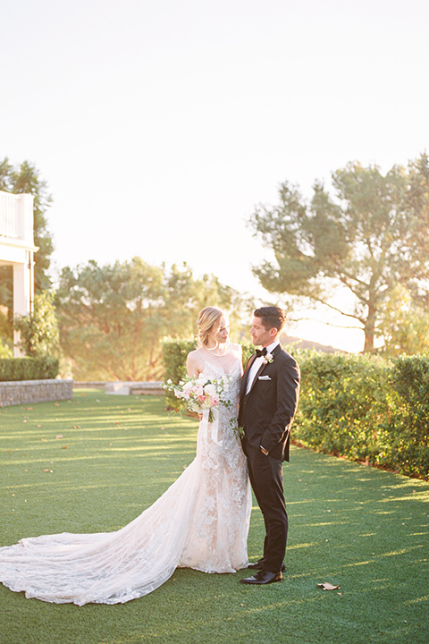  groom wearing black notch lapel tuxedo and the bride in a white fitted gown with a low back detail and lace accents