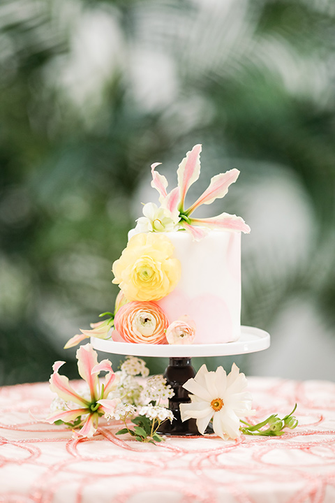  bride in a fashionable white jump suit with a strapless neckline and wide leg and the groom in a rose pink suit with a black floral neck tie