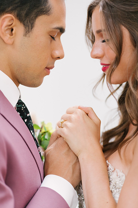  bride in a fashionable white jump suit with a strapless neckline and wide leg and the groom in a rose pink suit with a black floral neck tie