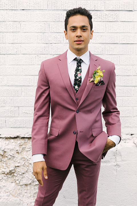  bride in a fashionable white jump suit with a strapless neckline and wide leg and the groom in a rose pink suit with a black floral neck tie