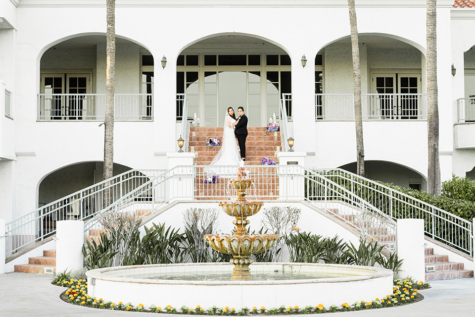  one bride in a black women’s tuxedo with a black diamond shaped bow tie and one bride in a white mermaid style gown with a beaded bodice and strapless neckline 