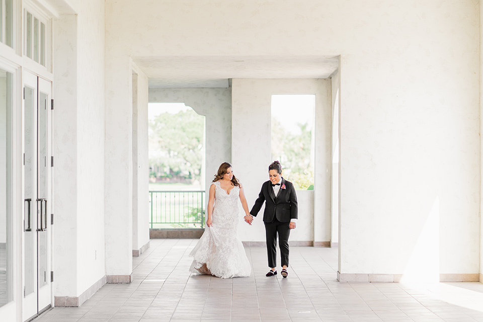  one bride in a black women’s tuxedo with a black diamond shaped bow tie and one bride in a white mermaid style gown with a beaded bodice and strapless neckline 