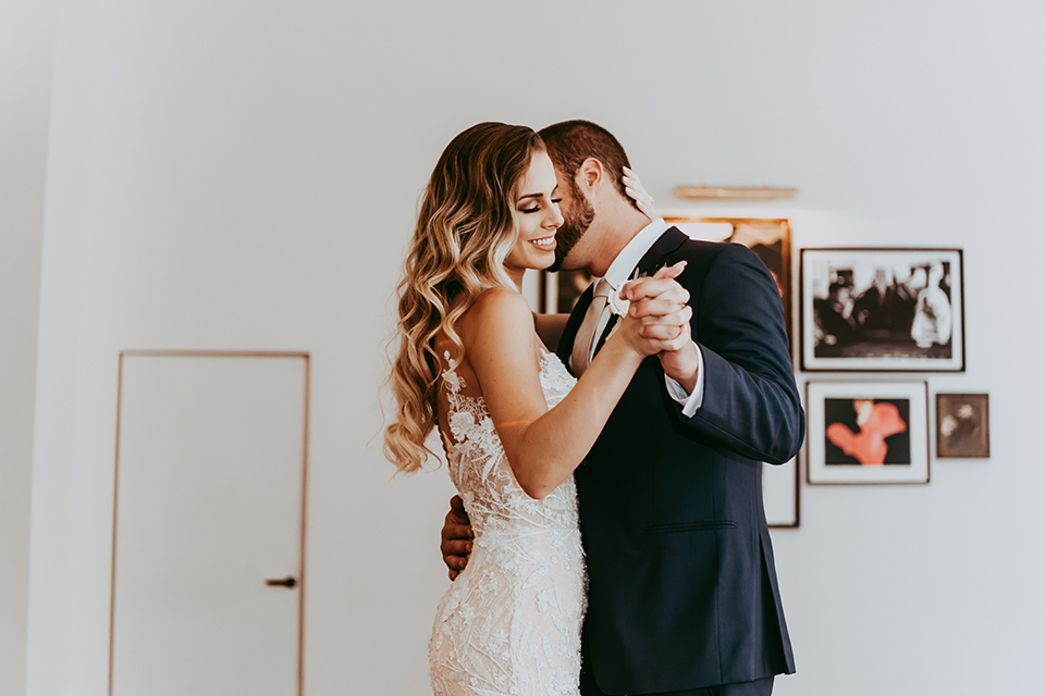  groom in a navy suit and bow tie and the bride in a white lace strapless gown dancing