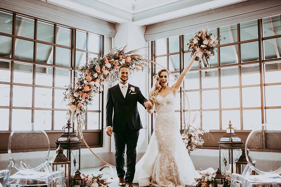  groom in a navy suit and bow tie and the bride in a white lace strapless gown walking down the aisle