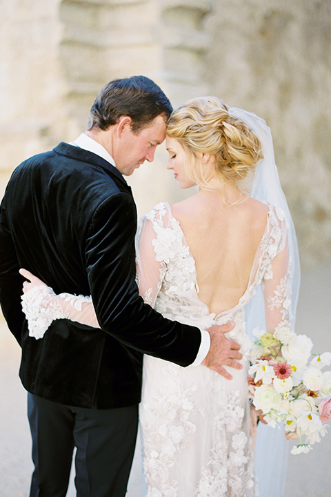  bride in a lace white gown with long illusion sleeves and the groom in a black velvet tuxedo
