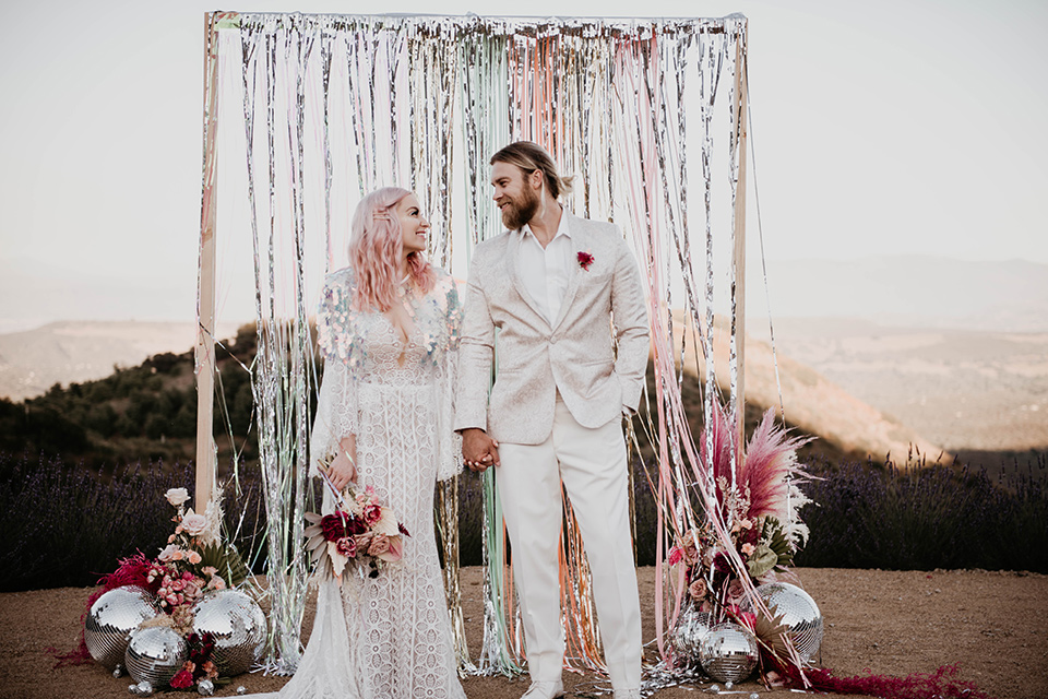  the bride in a fun sequin gown with a faux fur coat and the groom in an ivory paisley tuxedo 