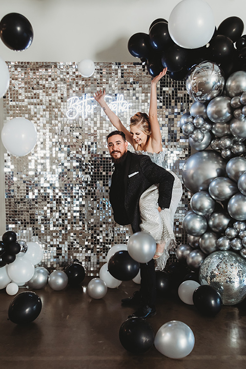  bride in a silver gown with her hair in a braided bun and the groom in an all-black suit 