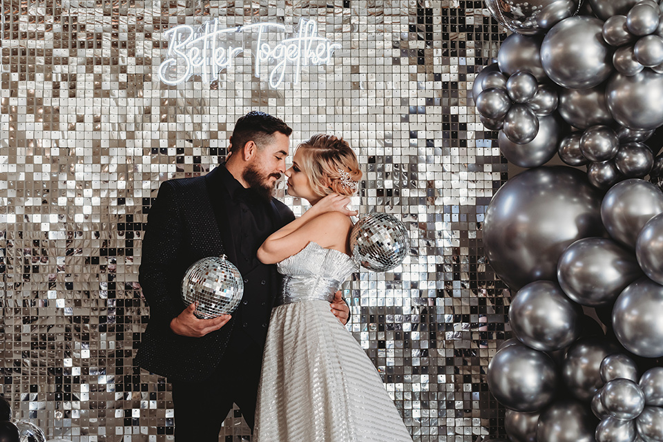  bride in a silver gown with her hair in a braided bun and the groom in an all-black suit 