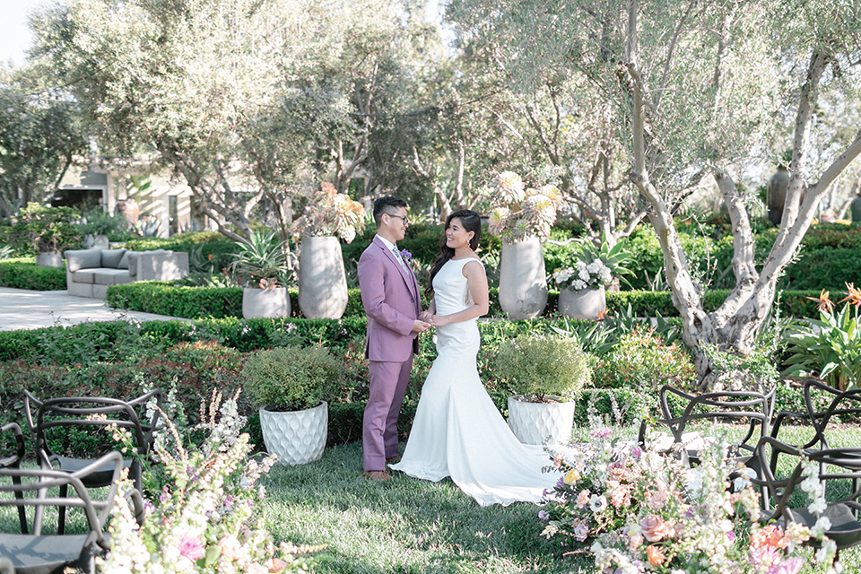  bride in a formfitting gown with a high neck and a long train groom in a rose pink suit and a light blue floral tie 