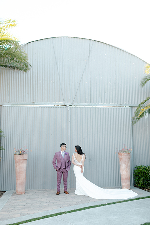  bride in a formfitting gown with a high neck and a long train groom in a rose pink suit and a light blue floral tie 