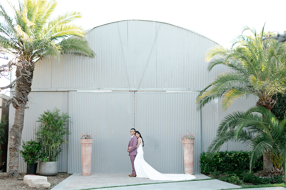  bride in a formfitting gown with a high neck and a long train groom in a rose pink suit and a light blue floral tie 