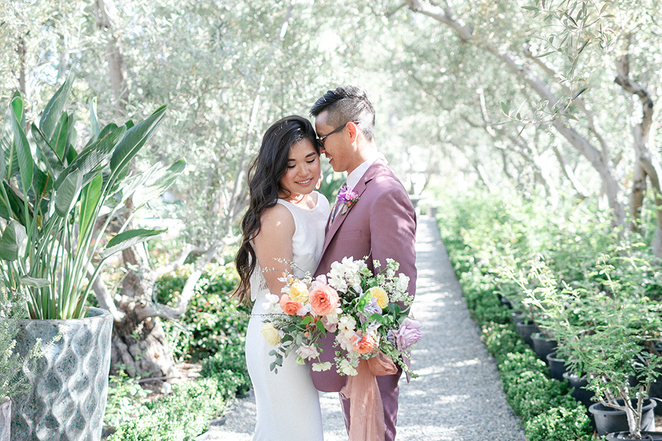  bride in a formfitting gown with a high neck and a long train groom in a rose pink suit and a light blue floral tie 