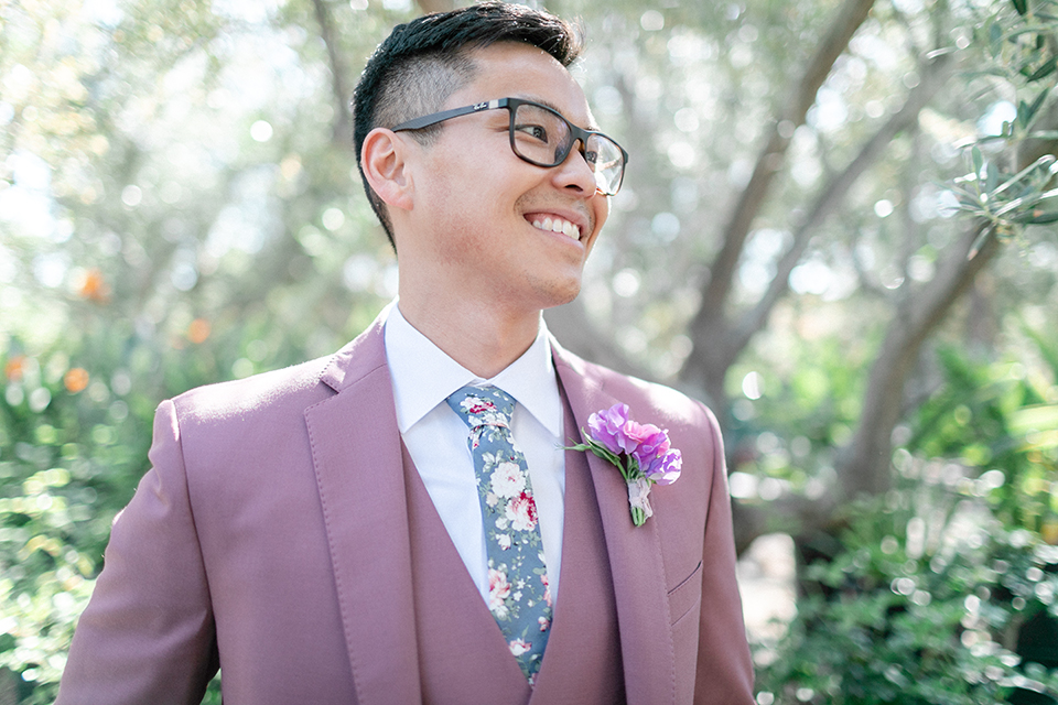  bride in a formfitting gown with a high neck and a long train groom in a rose pink suit and a light blue floral tie 