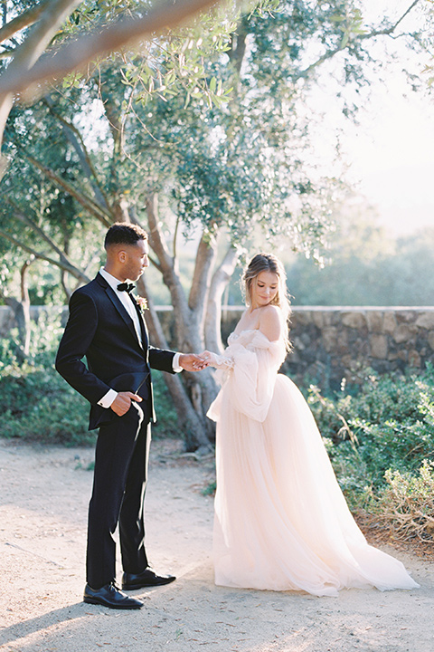  bride in a blush gown with off the shoulder sleeves and the groom in a black notch lapel tuxedo and black bow tie