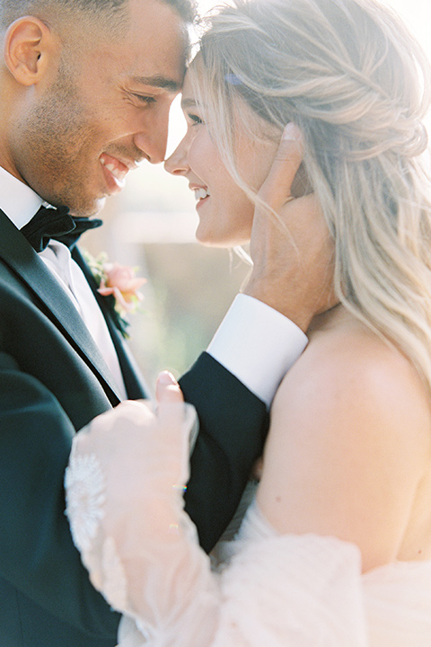  bride in a blush gown with off the shoulder sleeves and the groom in a black notch lapel tuxedo and black bow tie 