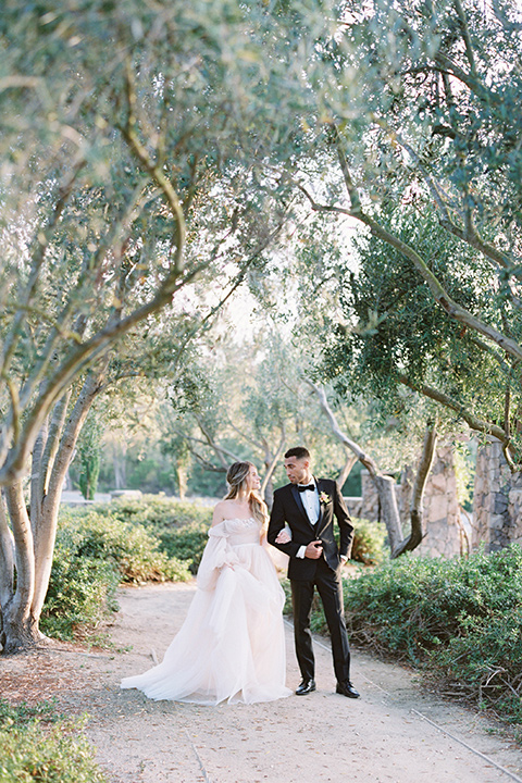  bride in a blush gown with off the shoulder sleeves and the groom in a black notch lapel tuxedo and black bow tie