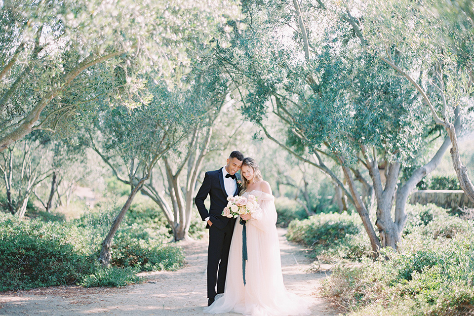  bride in a blush gown with off the shoulder sleeves and the groom in a black notch lapel tuxedo and black bow tie 