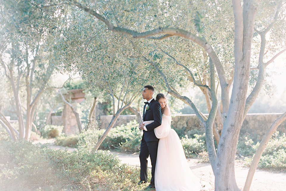  bride in a blush gown with off the shoulder sleeves and the groom in a black notch lapel tuxedo and black bow tie 