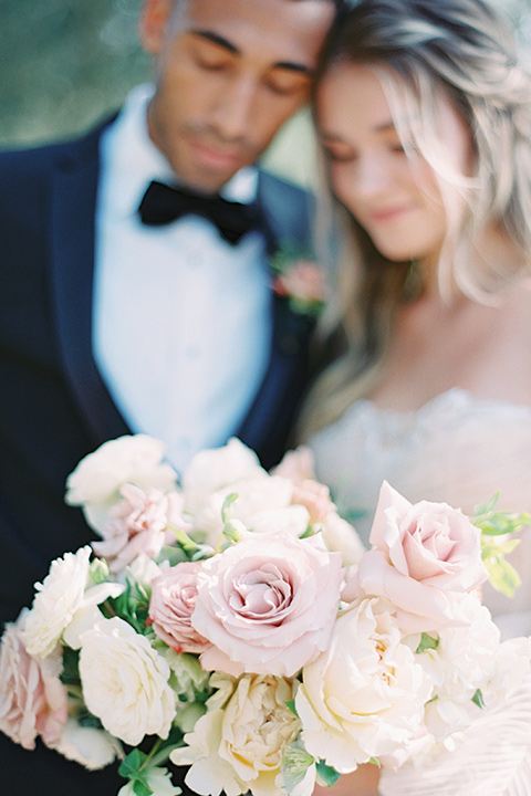  bride in a blush gown with off the shoulder sleeves and the groom in a black notch lapel tuxedo and black bow tie