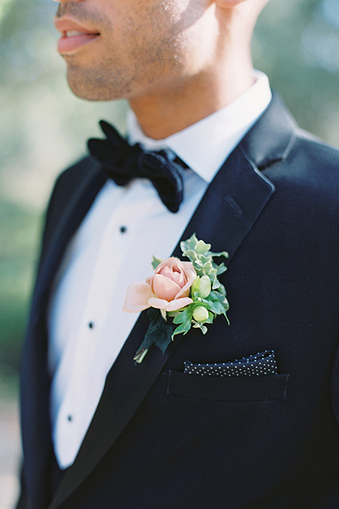  bride in a blush gown with off the shoulder sleeves and the groom in a black notch lapel tuxedo and black bow tie 