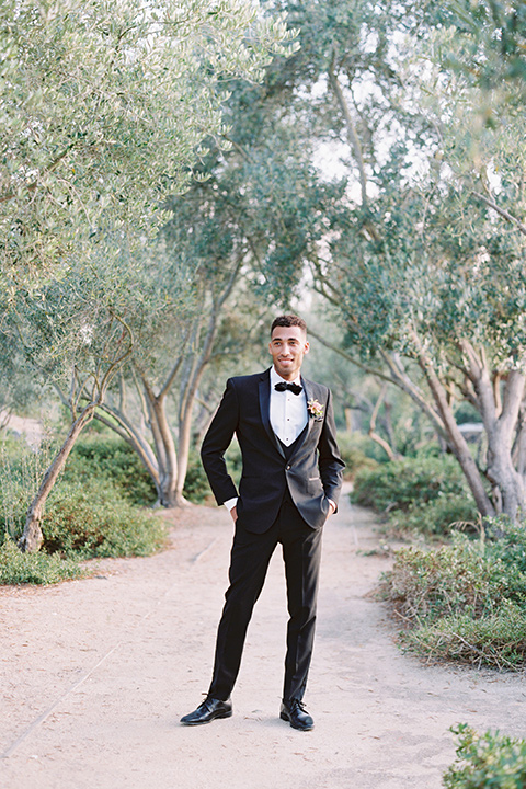  bride in a blush gown with off the shoulder sleeves and the groom in a black notch lapel tuxedo and black bow tie