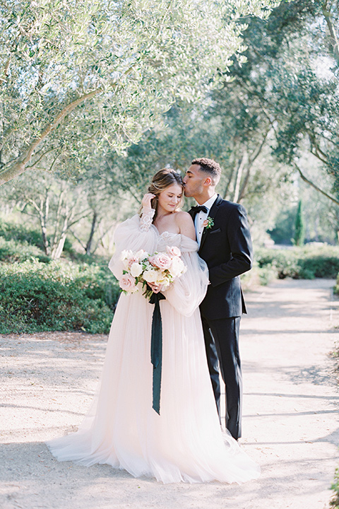  bride in a blush gown with off the shoulder sleeves and the groom in a black notch lapel tuxedo and black bow tie 