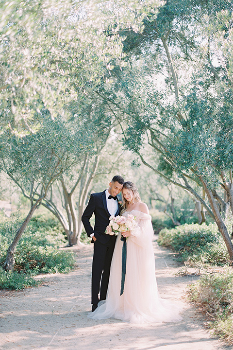  bride in a blush gown with off the shoulder sleeves and the groom in a black notch lapel tuxedo and black bow tie