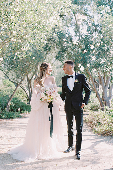  bride in a blush gown with off the shoulder sleeves and the groom in a black notch lapel tuxedo and black bow tie 