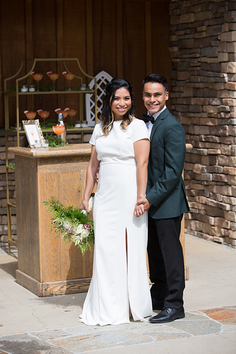  bride in a modern formfitting gown with cap sleeves and a high neck and the groom in a green suit with a floral tie