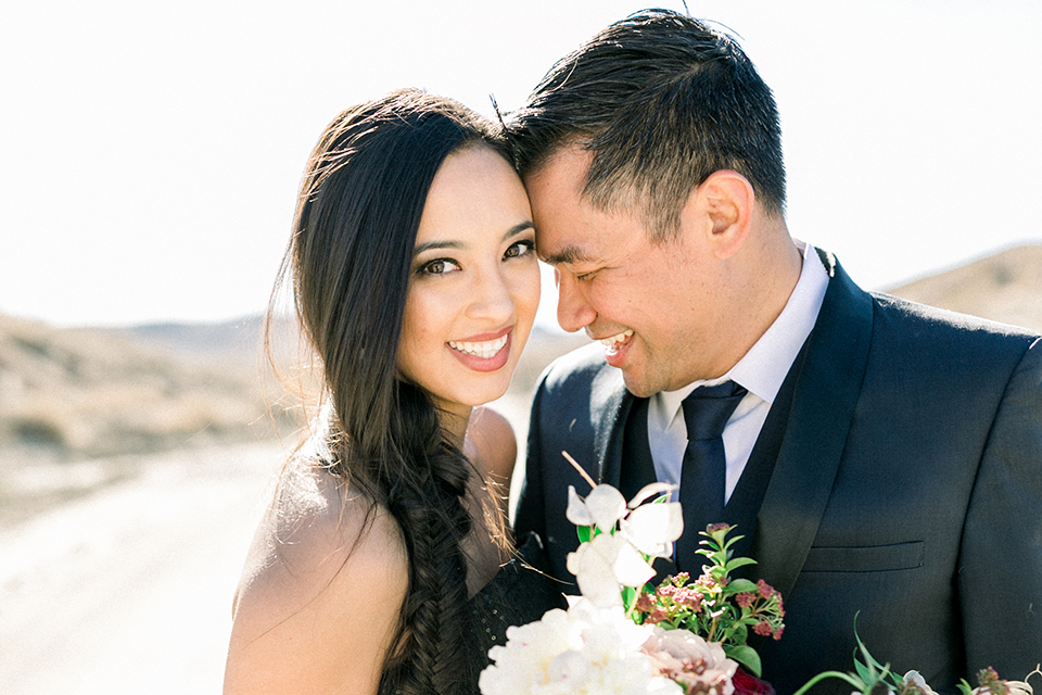  bride in a black jumpsuit with a tulle overlay and the groom in a navy shawl lapel tuxedo with a black long tie 