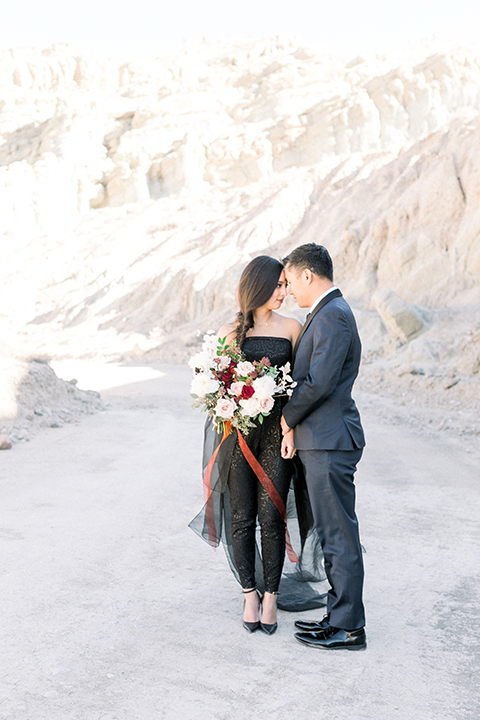  bride in a black jumpsuit with a tulle overlay and the groom in a navy shawl lapel tuxedo with a black long tie 