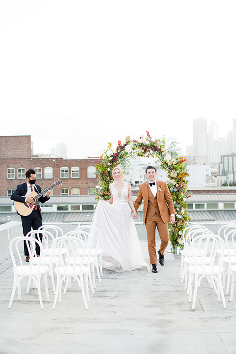  the bride in a white gown with an illusion neckline and hair in a low bun, the groom in a caramel brown suit with a chocolate brown bow tie 